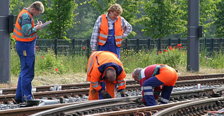 Bauarbeiter in orangener Arbeitskleidung beim Arbeiten an den Schienen