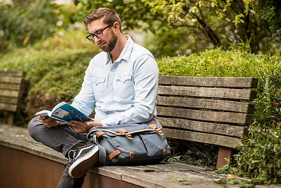 Mann mit Brille auf einer Holzbank im Park beim Lesen der VGF-Fahrpläne und VGF-Preise