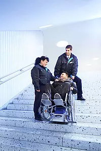 Zwei VGF-Fahrgastbetreuer helfen einem Mann im Rollstuhl auf den Treppen