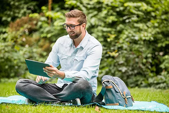 [Translate to English:] Student mit Tablet im Park auf der Picknickdecke
