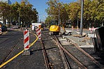 Gelber Bagger auf Schienen an einer Baustelle mit Absperrpfosten