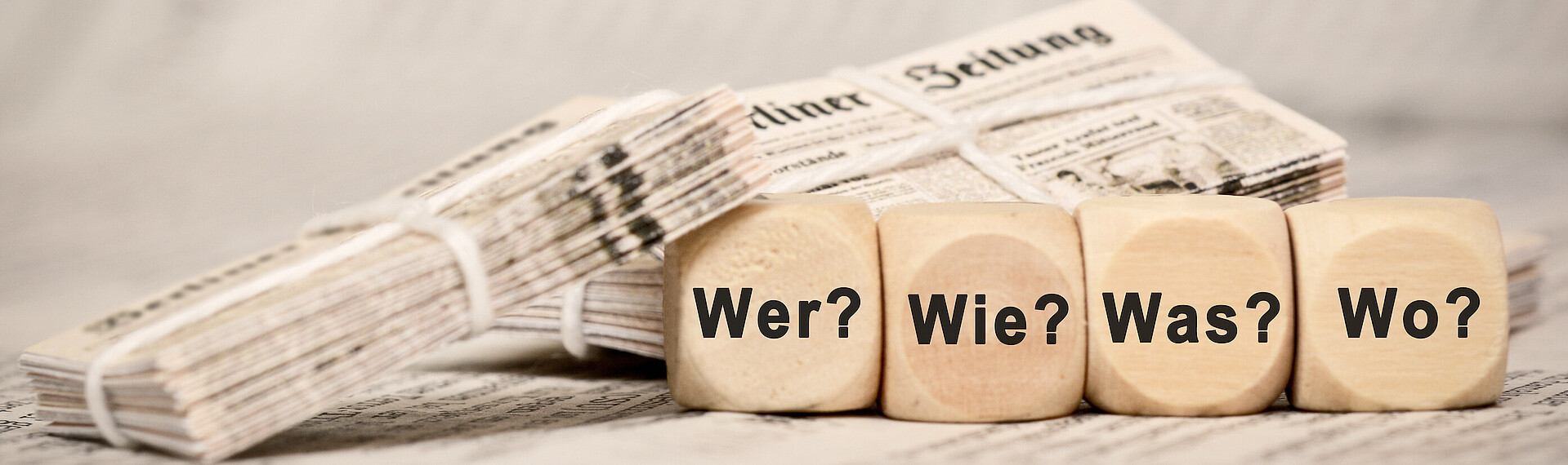 Zeitungen im Bild und Holzwürfel mit den Fragen Wer, Wie, Was, Wo