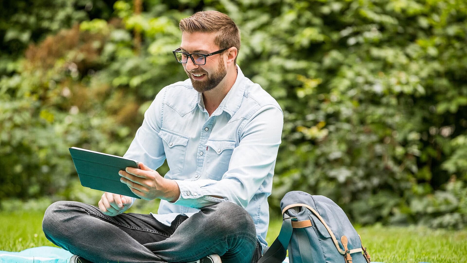 [Translate to English:] Student sitzt auf der Wiese und arbeitet etwas für die Uni aus.