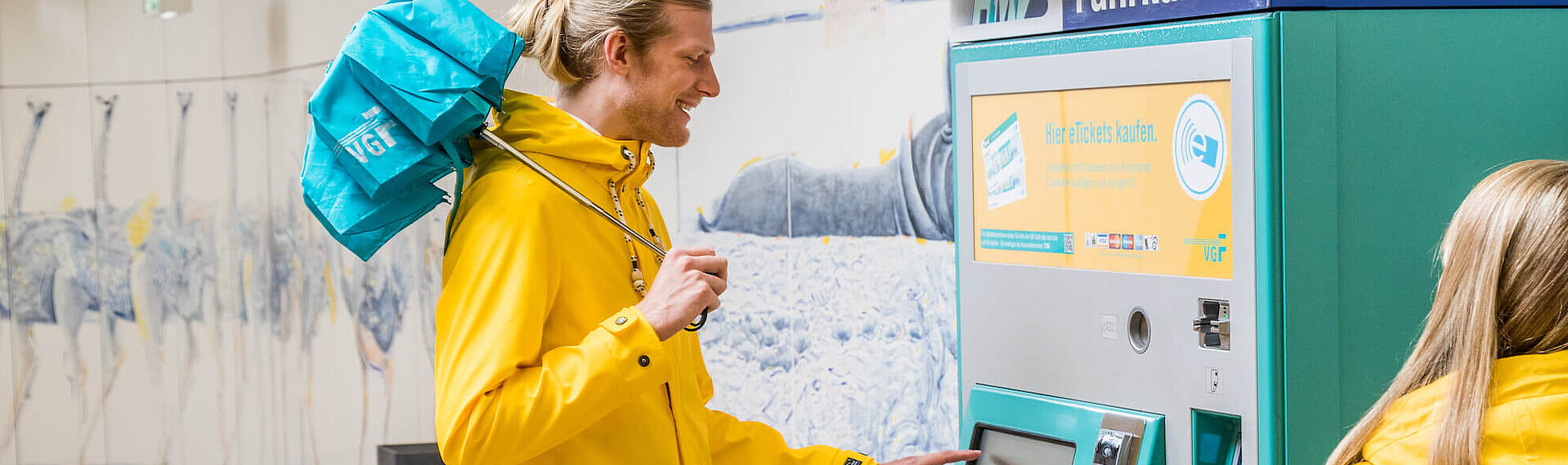 Casual rider with raincoat and umbrella buys a weekly ticket at the ticket machine.