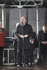 Mann vor einem Mikro im schwarzen Business-Anzug