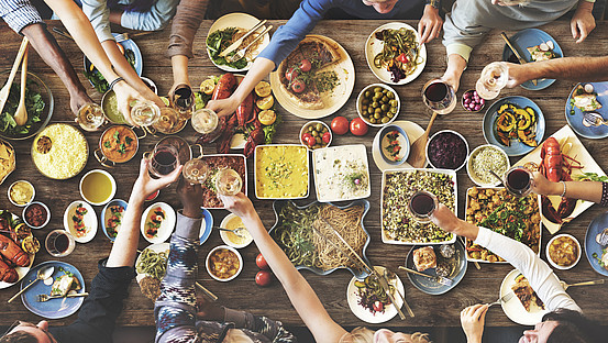 Verschiedene Hände von Menschen mit Essen auf dem Tisch beim Anstoßen