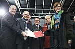 Männer und Frau auf einer Bühne zur Kamera schauend mit einem Dokument in der Hand