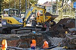 Gelber Bagger bei der Arbeit eines Straßenaufbruchs mit Bauarbeitern