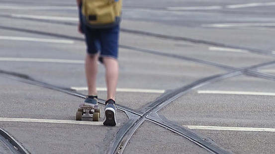 Junge mit Skateboard, der inmitten von Straßenbahnschienen fährt