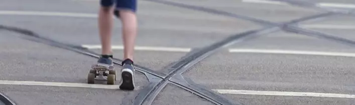 Junge mit Skateboard, der inmitten von Straßenbahnschienen fährt