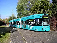 VGF-Bahn beim schönen Wetter mit Bäumen und Wiese rechts und links der Schienen