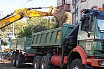Grüner Container LKW in dem ein Bagger etwas reinwirft