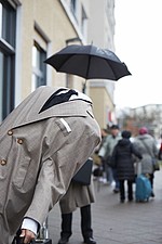 Grauer Mantel mit schwarzem Schirm im Regen draussen