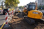Gelber Bagger beim Straßenaufbruch mit Absperrpfosten