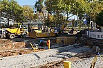 Straßenbaustelle mit Baugeräten und grünen Bäumen im Hintergrund