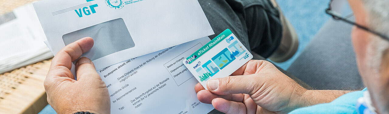 Mann mit Brille, der den Frankfurt-Pass in der Hand hält mit dem VGF-Briefumschlag.