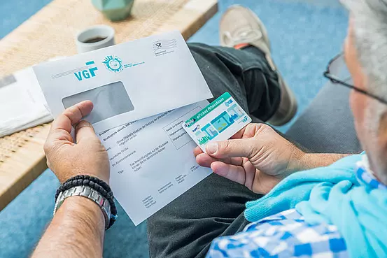 Mann mit Brille, der den Frankfurt-Pass in der Hand hält mit dem VGF-Briefumschlag.