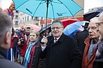 Mann mit schwarzem Mantel und einem geöffneten VGF-Regenschirm inmitten einer Menschenmenge
